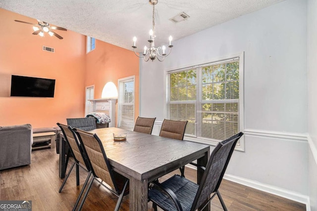 dining room with ceiling fan with notable chandelier, a high ceiling, a textured ceiling, and hardwood / wood-style flooring