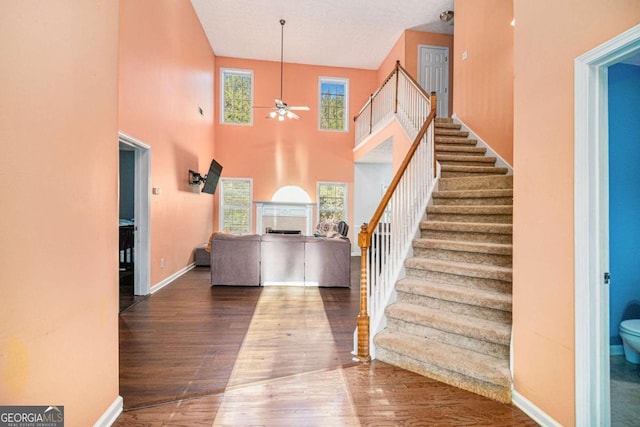 stairway with a high ceiling, ceiling fan, and wood-type flooring