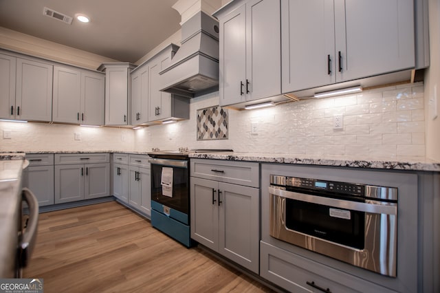 kitchen featuring premium range hood, light stone countertops, light wood-type flooring, and appliances with stainless steel finishes