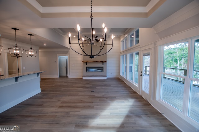 unfurnished living room featuring a large fireplace, dark hardwood / wood-style flooring, a tray ceiling, and a chandelier