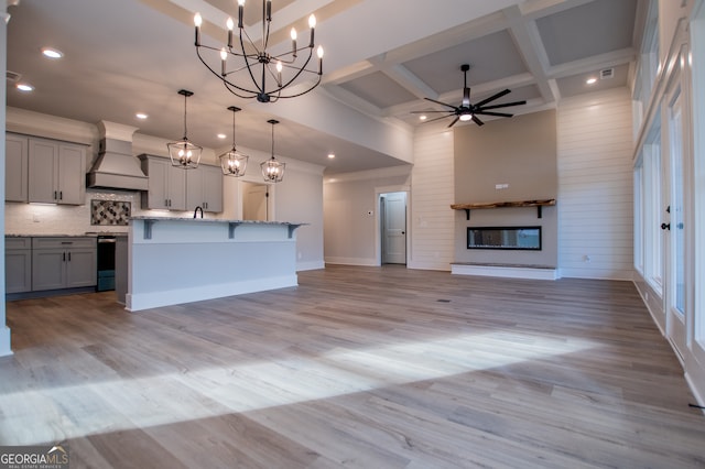 kitchen featuring gray cabinetry, custom range hood, a kitchen island with sink, decorative light fixtures, and light hardwood / wood-style flooring