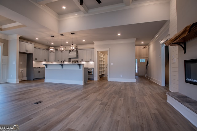 kitchen featuring a center island with sink, ornamental molding, decorative light fixtures, and light wood-type flooring