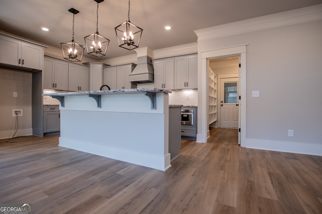 kitchen featuring stainless steel oven, light stone counters, pendant lighting, a kitchen bar, and hardwood / wood-style flooring