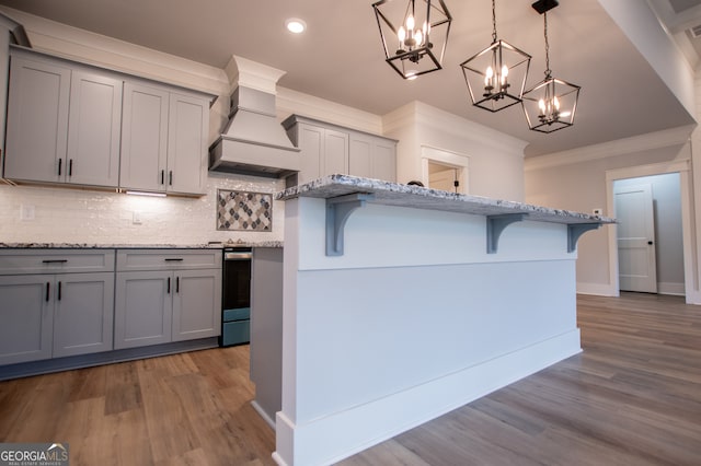 kitchen with custom range hood, hardwood / wood-style flooring, crown molding, decorative light fixtures, and gray cabinets