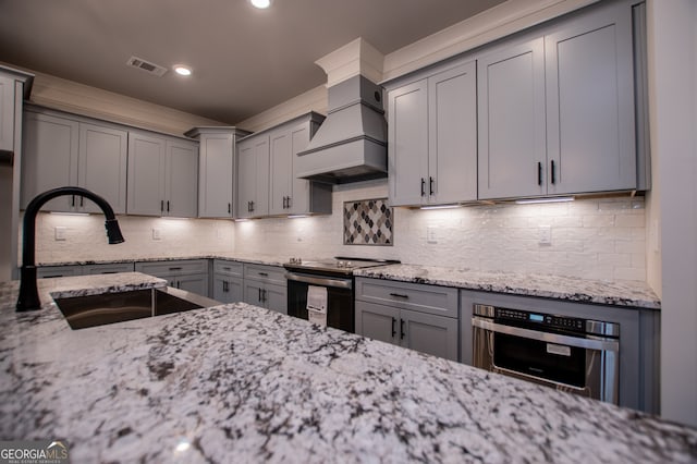 kitchen featuring sink, stainless steel appliances, light stone counters, decorative backsplash, and custom exhaust hood