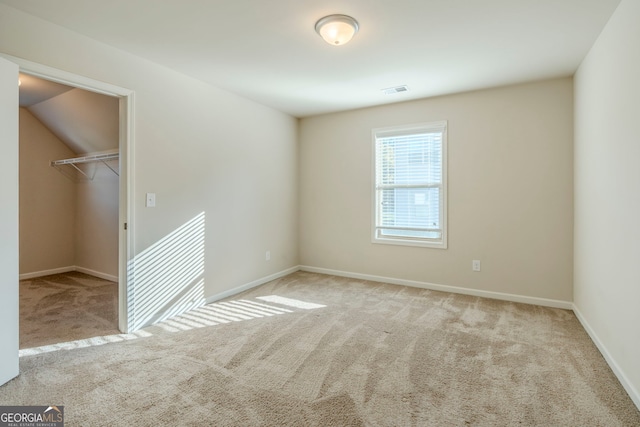 unfurnished bedroom featuring a walk in closet, a closet, and light colored carpet