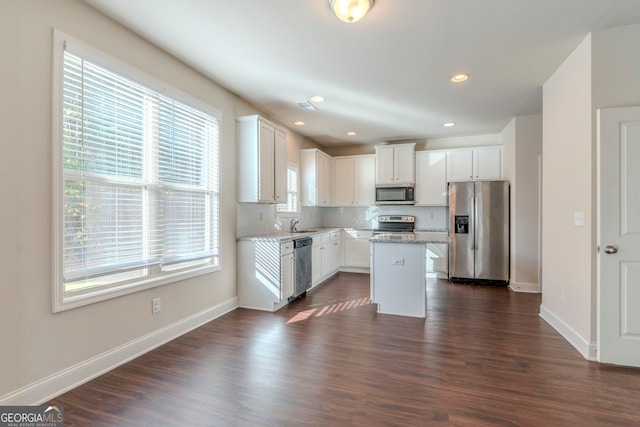 kitchen with white cabinetry, light stone countertops, a kitchen island, dark hardwood / wood-style flooring, and appliances with stainless steel finishes