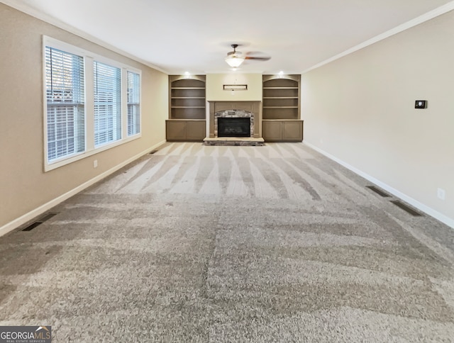 unfurnished living room featuring built in shelves, ceiling fan, crown molding, and carpet floors