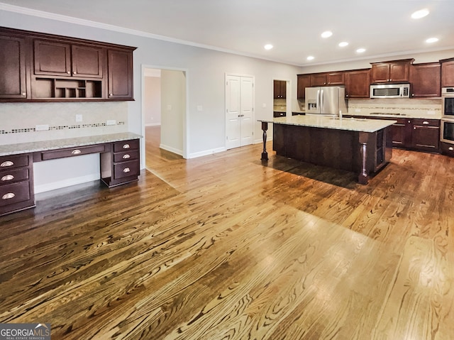 kitchen featuring backsplash, an island with sink, dark wood-type flooring, and appliances with stainless steel finishes