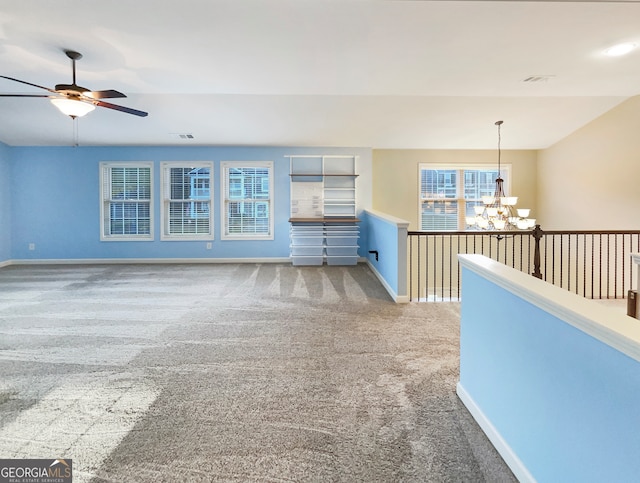 carpeted spare room featuring ceiling fan with notable chandelier