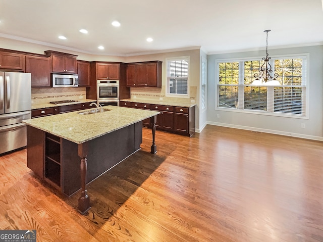 kitchen with light stone countertops, hardwood / wood-style floors, stainless steel appliances, and a center island with sink