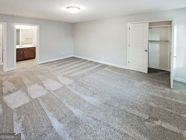 unfurnished bedroom with a closet, ensuite bathroom, and light carpet