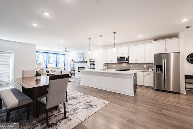 kitchen featuring an island with sink, stainless steel appliances, decorative light fixtures, and wood-type flooring