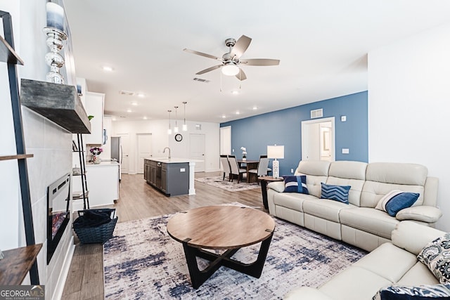 living room featuring a tiled fireplace, ceiling fan, sink, and light hardwood / wood-style floors