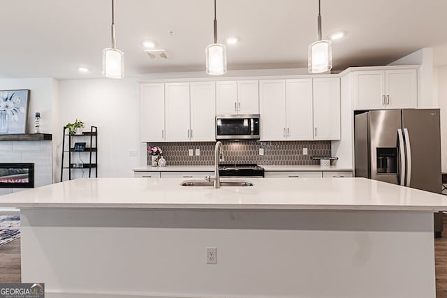 kitchen featuring sink, dark wood-type flooring, decorative light fixtures, a center island with sink, and appliances with stainless steel finishes