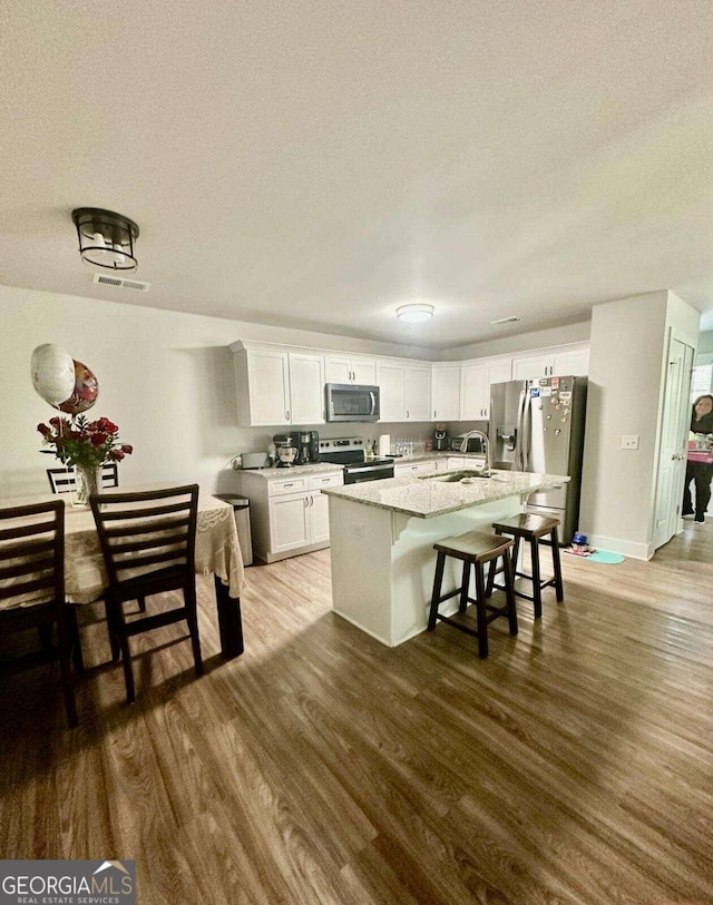 kitchen with a kitchen bar, white cabinetry, stainless steel appliances, hardwood / wood-style flooring, and a center island with sink