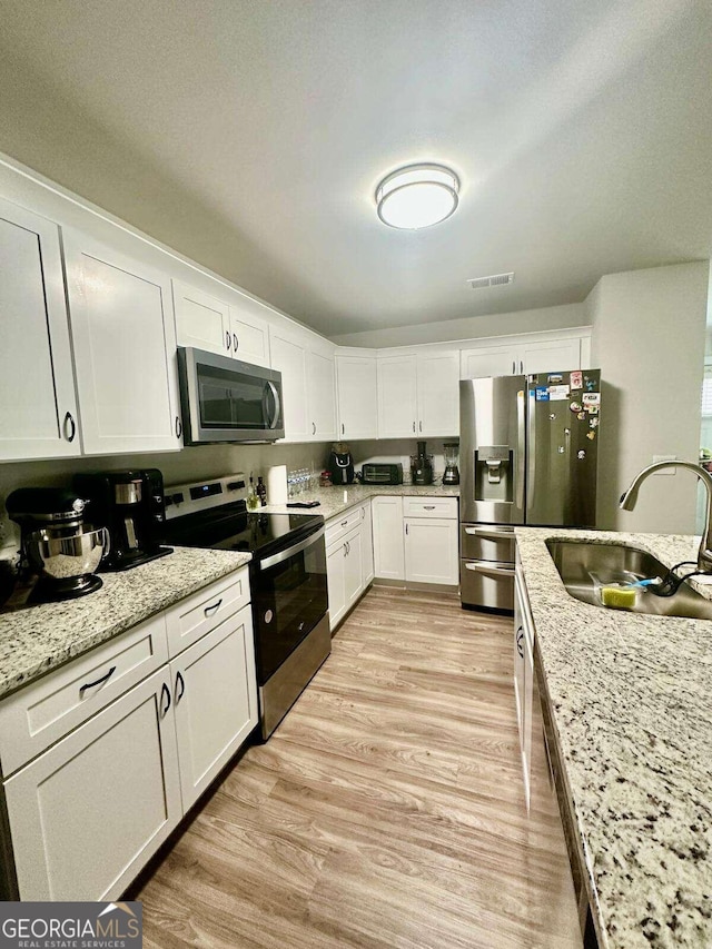 kitchen featuring light stone countertops, white cabinets, stainless steel appliances, sink, and light wood-type flooring