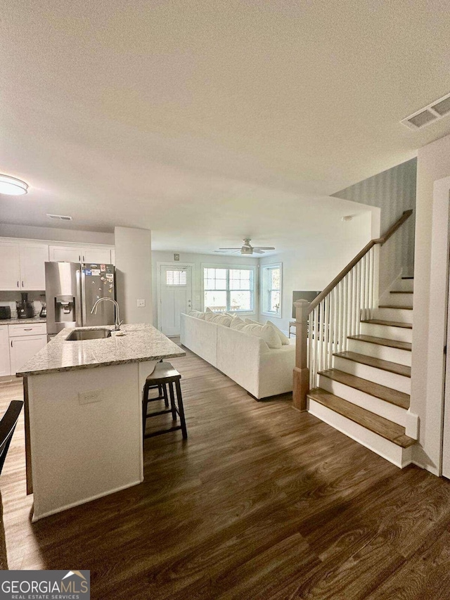 kitchen featuring stainless steel fridge with ice dispenser, a kitchen bar, an island with sink, light stone countertops, and white cabinets