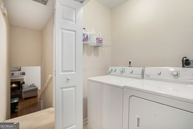 washroom with laundry area, a lit fireplace, visible vents, and washing machine and clothes dryer