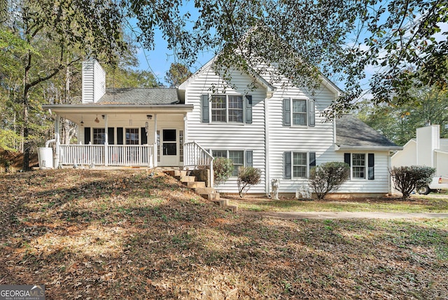 rear view of property with covered porch, roof with shingles, and a chimney