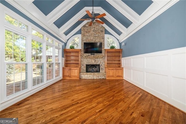 unfurnished living room featuring vaulted ceiling with beams, hardwood / wood-style flooring, crown molding, ceiling fan, and a stone fireplace