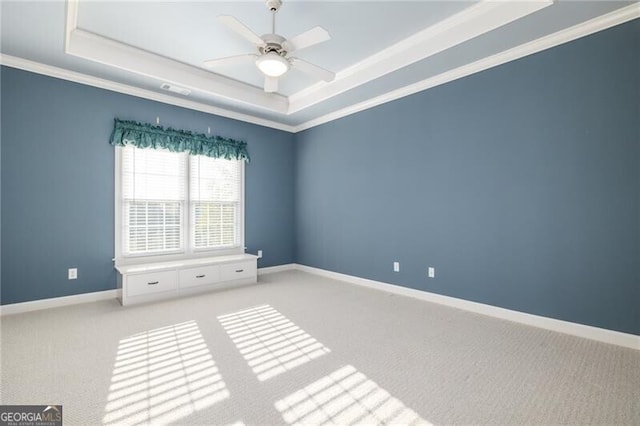 empty room featuring a raised ceiling, ceiling fan, light carpet, and ornamental molding