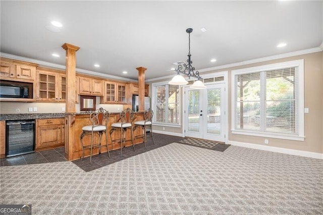 kitchen with beverage cooler, dark colored carpet, light stone counters, decorative columns, and a breakfast bar area