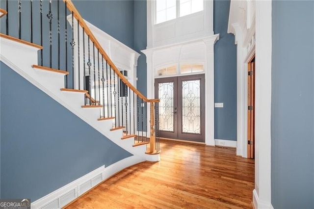 entryway with french doors, a towering ceiling, and wood-type flooring