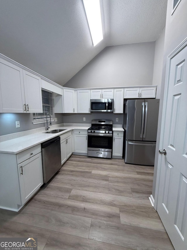 kitchen featuring light hardwood / wood-style flooring, white cabinetry, sink, lofted ceiling, and stainless steel appliances