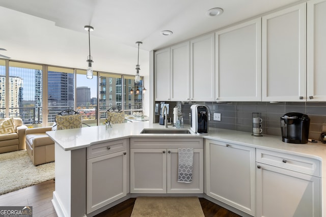 kitchen featuring kitchen peninsula, dark wood-type flooring, sink, pendant lighting, and white cabinets