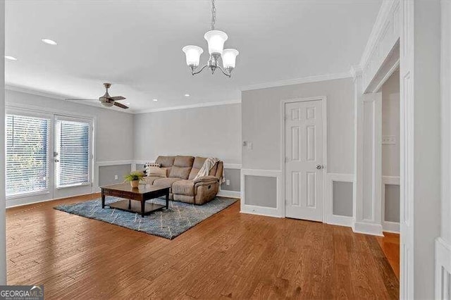 living room with ceiling fan with notable chandelier, wood-type flooring, and crown molding