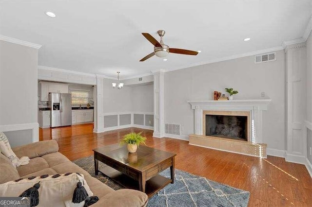 living room with a tile fireplace, ceiling fan with notable chandelier, hardwood / wood-style flooring, and crown molding