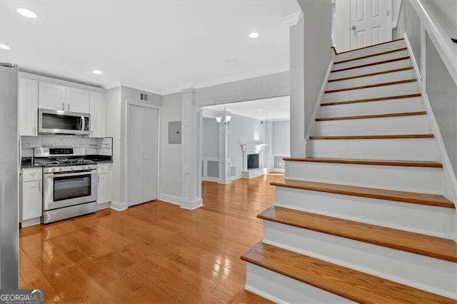 kitchen with appliances with stainless steel finishes, light hardwood / wood-style flooring, white cabinetry, and ornamental molding