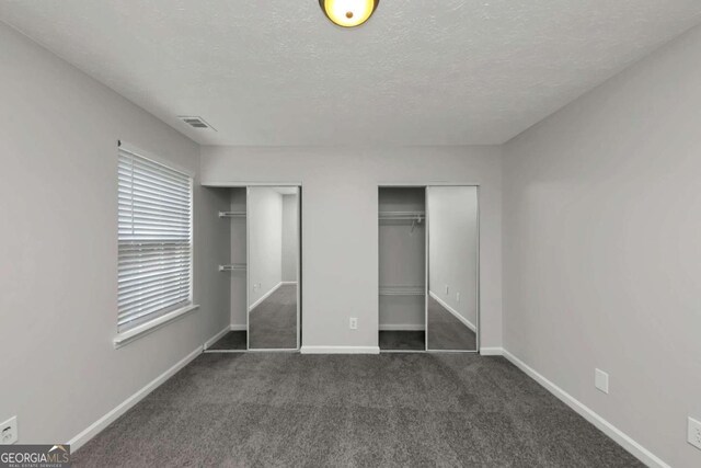 unfurnished bedroom featuring dark carpet, multiple closets, and a textured ceiling