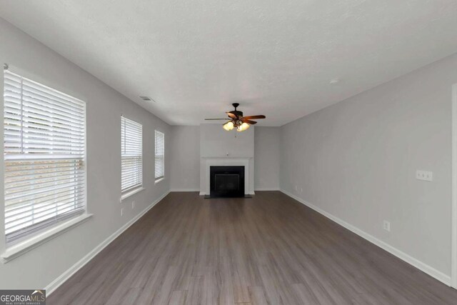 unfurnished living room with ceiling fan, dark hardwood / wood-style floors, and a textured ceiling