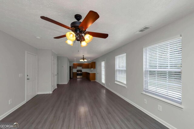 unfurnished living room with ceiling fan with notable chandelier, dark wood-type flooring, and a textured ceiling