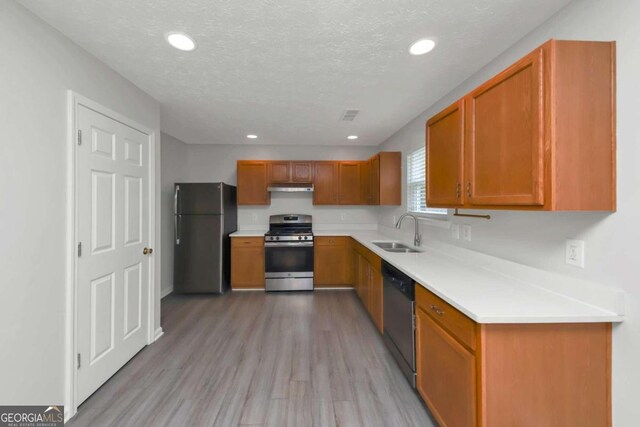 kitchen with a textured ceiling, light wood-type flooring, stainless steel appliances, and sink