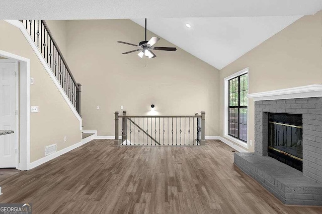 unfurnished living room featuring a brick fireplace, ceiling fan, wood-type flooring, and high vaulted ceiling