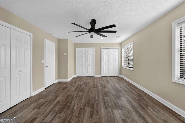 unfurnished bedroom featuring a textured ceiling, ceiling fan, dark wood-type flooring, and multiple closets