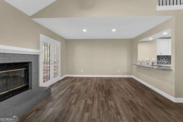 unfurnished living room featuring french doors, dark wood-type flooring, and a brick fireplace