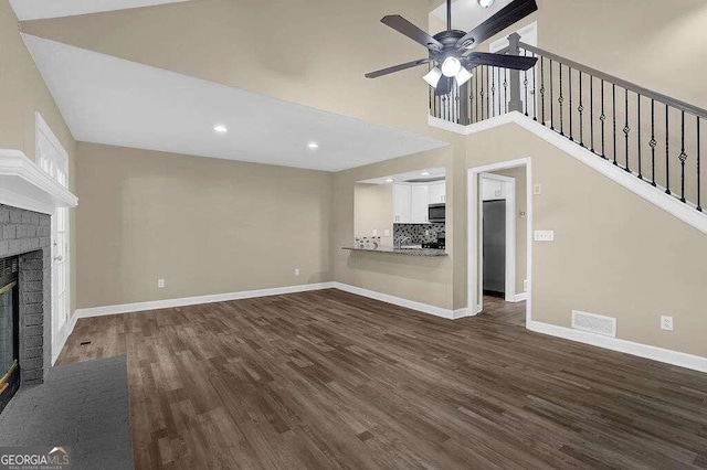 unfurnished living room featuring a fireplace, a high ceiling, dark hardwood / wood-style flooring, and ceiling fan