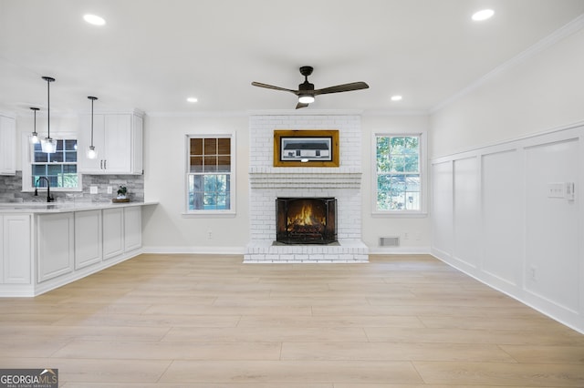 unfurnished living room with crown molding, a fireplace, visible vents, a decorative wall, and a sink