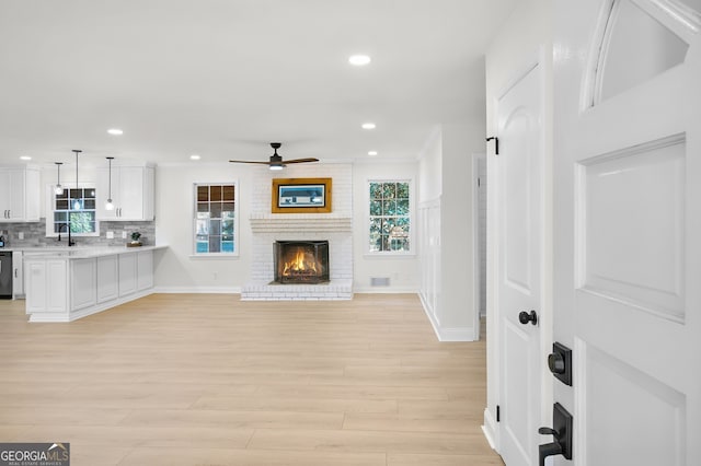 living room featuring ceiling fan, sink, a fireplace, and light hardwood / wood-style flooring