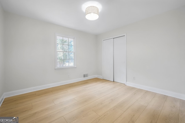 unfurnished bedroom with a closet, visible vents, baseboards, and wood finished floors