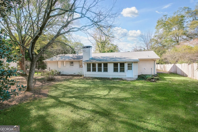 rear view of property with a chimney, fence, a lawn, and brick siding