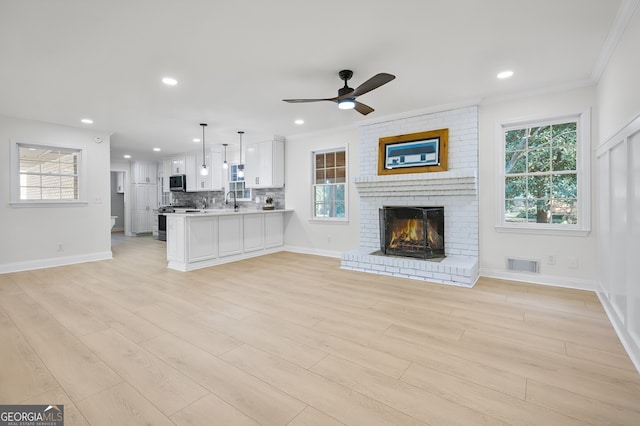 unfurnished living room with a brick fireplace, ornamental molding, ceiling fan, sink, and light hardwood / wood-style flooring