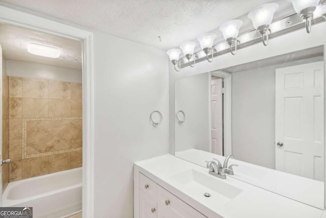 bathroom with vanity, a textured ceiling, and tiled shower / bath