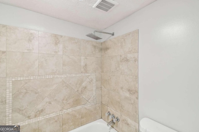 bathroom with tiled shower / bath combo and toilet