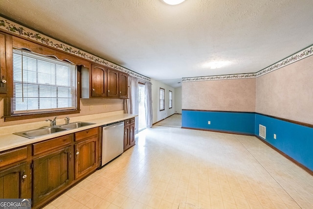 kitchen with a textured ceiling, stainless steel dishwasher, and sink