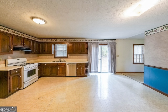 kitchen with white gas stove, stainless steel dishwasher, a textured ceiling, and sink